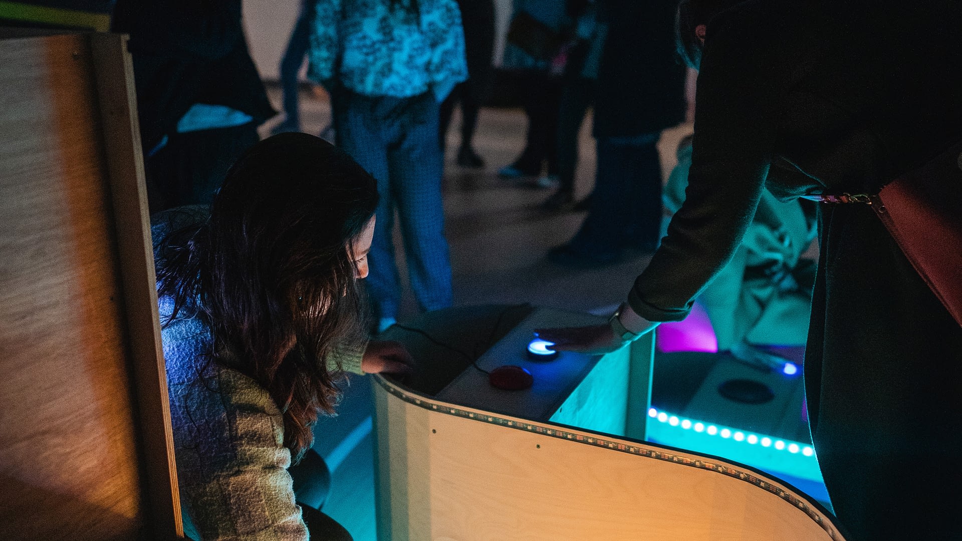 People play with buttons on a structure with LED lights that is shaped in the form of a sine wave